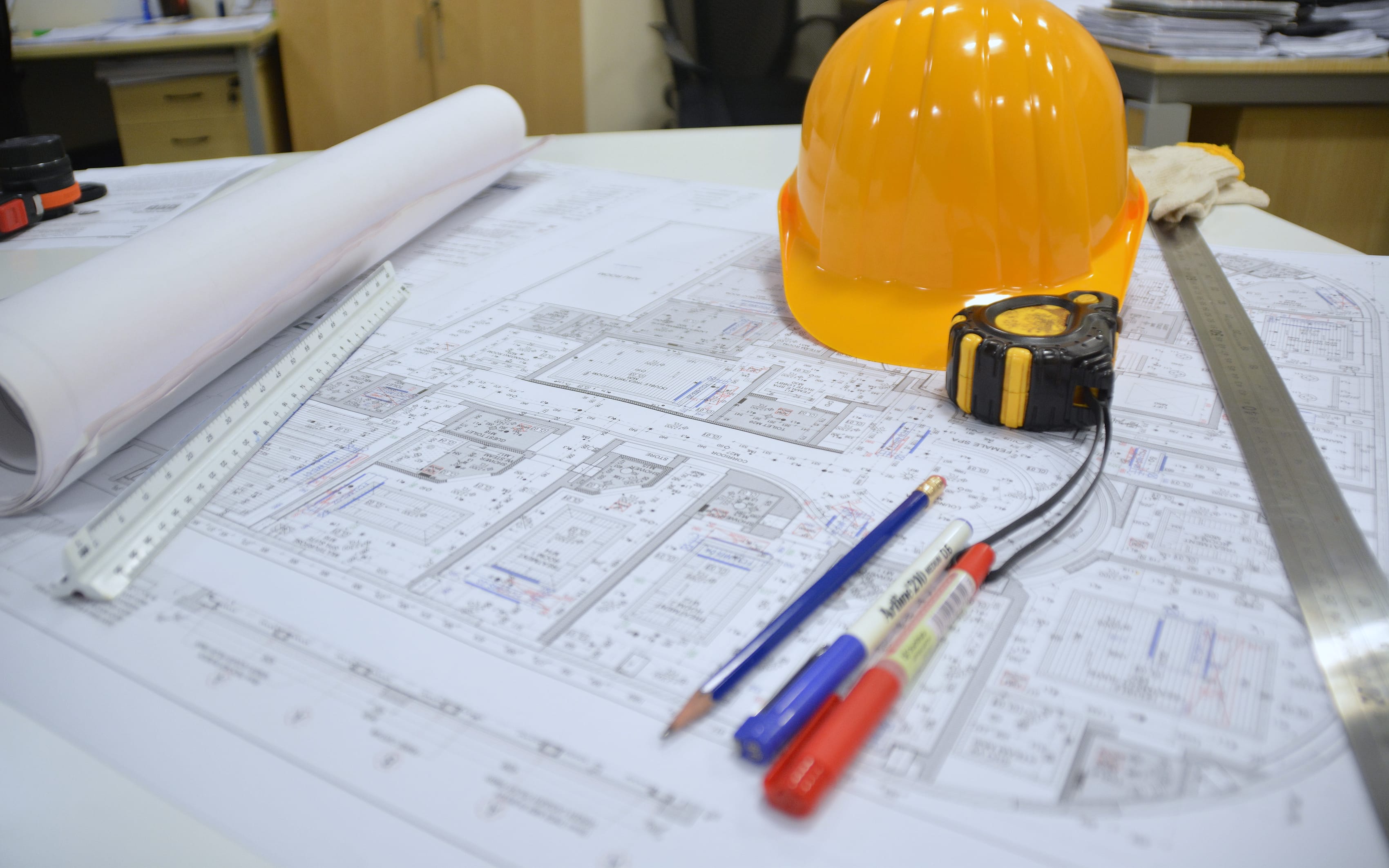 Drawings, a hard hat and a tape measure on a desk